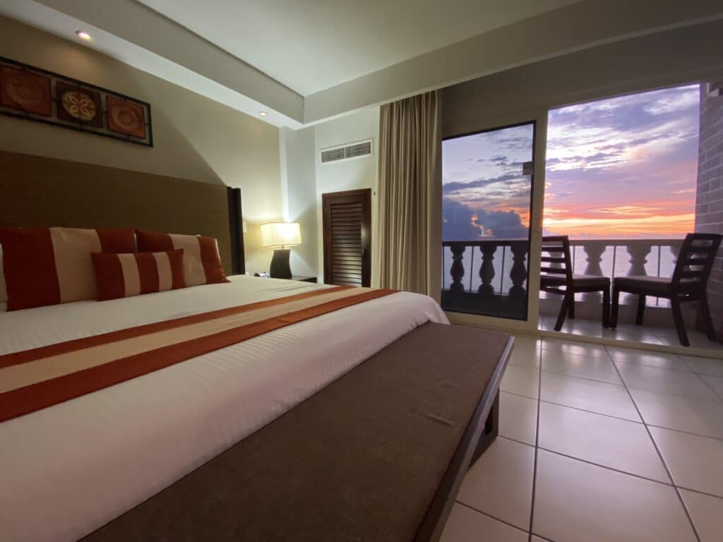 Cozy hotel room with ocean-view balcony at sunset.