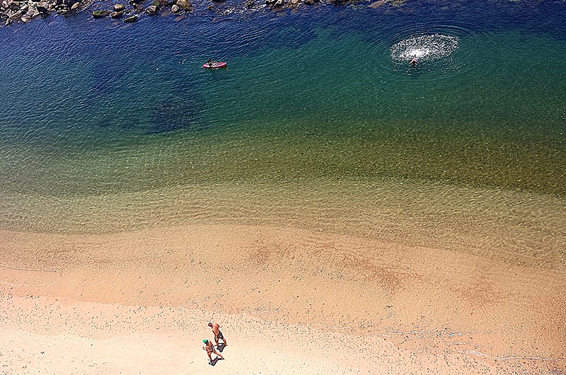 Aerial view of two people walking on the beach and two people swimming in the clear water.