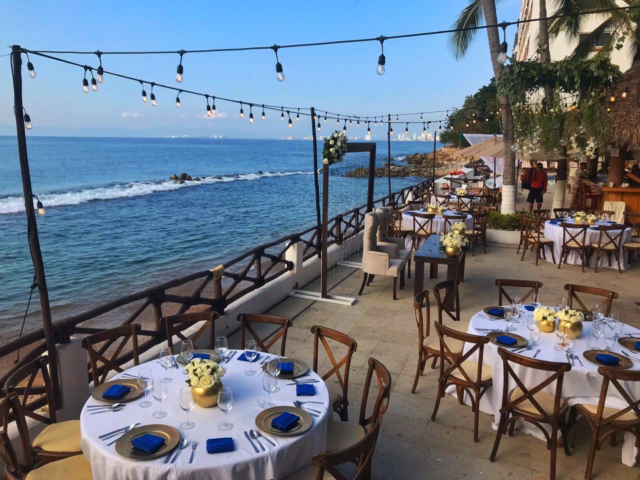 An outdoor wedding reception with round tables, string lights, and stunning ocean views.