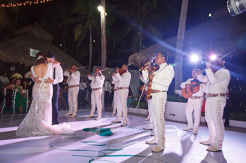 A mariachi band playing music while a newly wed couple dance.