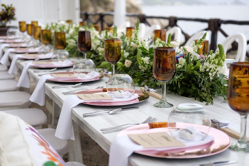 A closeup of a wedding reception long table decorated with a garland centerpiece and vintage colored wine glasses.