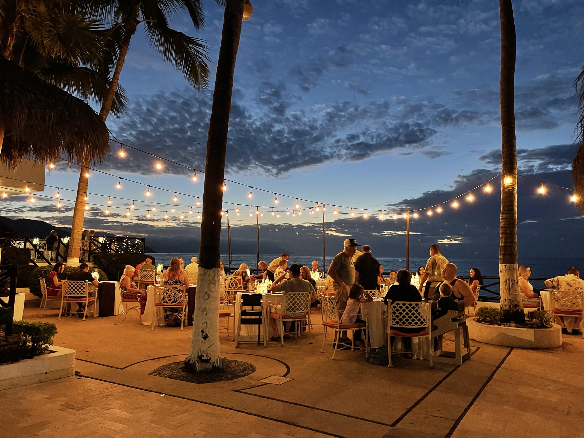 Evening outdoor dining with string lights and ocean.