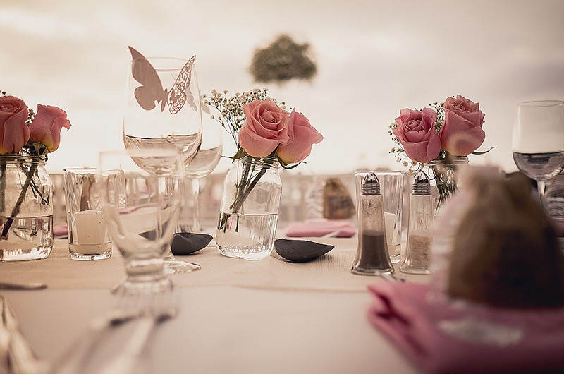 Focus on wedding reception table decorations with jars of pink roses and decorative butterflies on wine glasses.