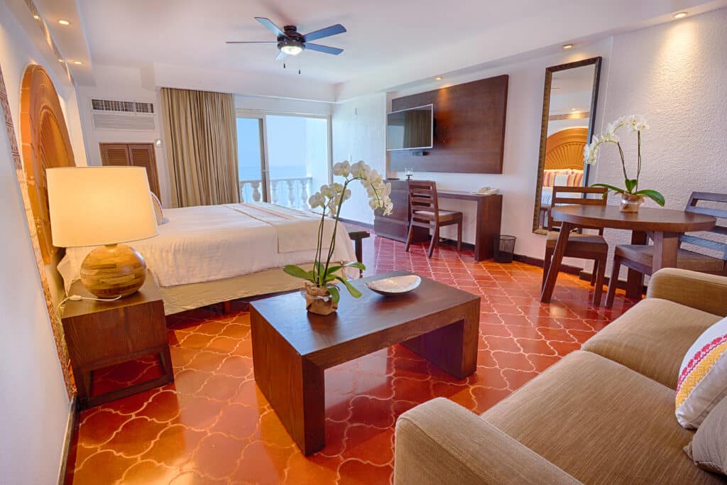 single-bed hotel room with orange accents, seating area and small dining table.