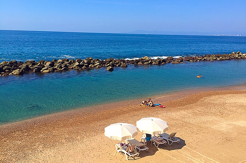 Two lounge chairs with umbrellas on the beach overlooking the clear water.