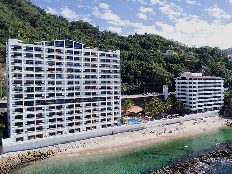 Two hotel buildings with beachfront access and mountain with trees on them behind the buildings.