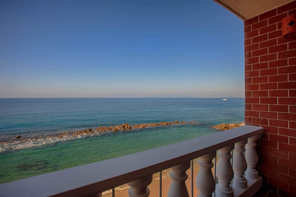 Ocean view from a red-brick balcony, clear skies above.