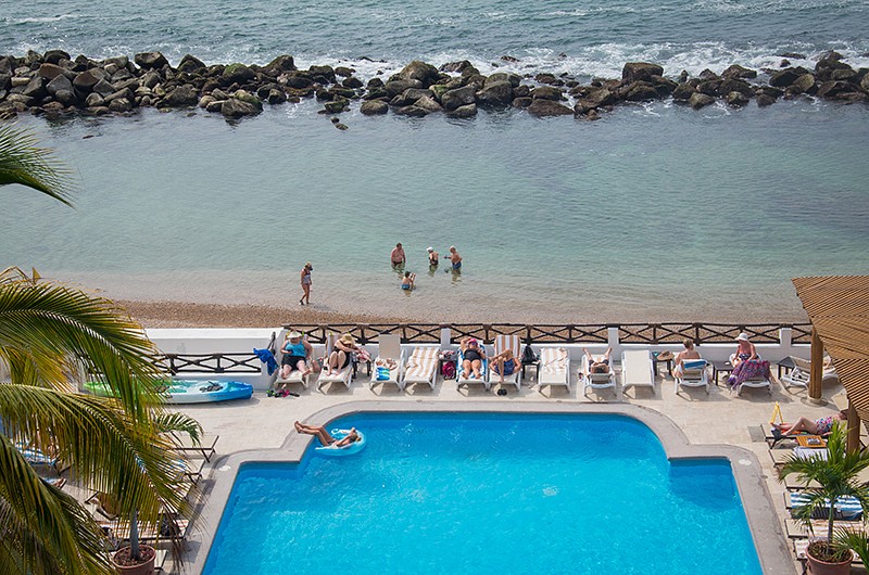 Aerial view of people relaxing by the pool and people at the beach.