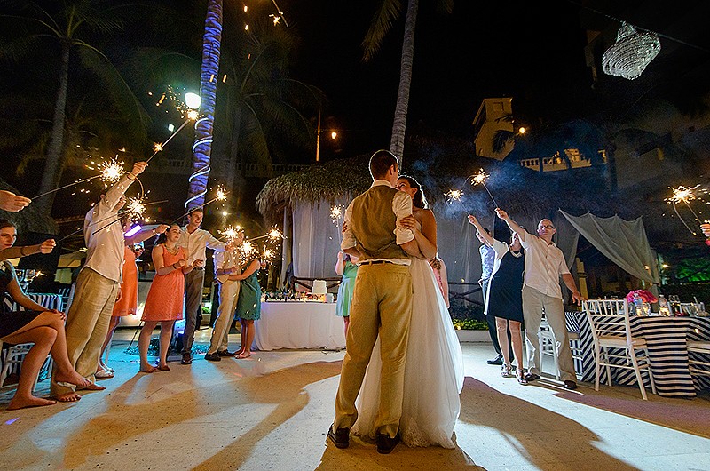 Couple slow dancing around guests holding sparklers.