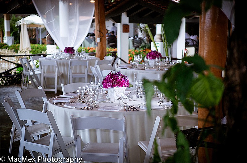 A wedding reception with white round tables and chairs and pink flower centerpieces.