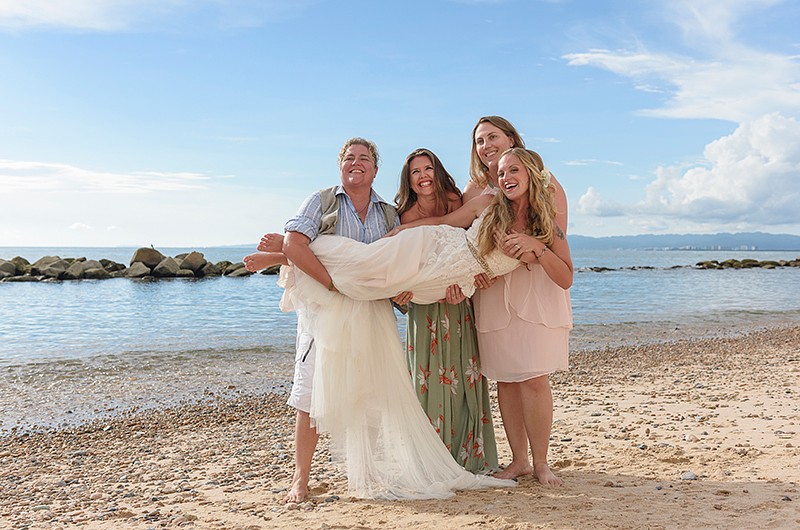 three guests holding up the bride for a photo on the beach.