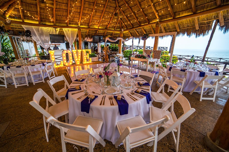 An covered outdoor wedding reception with round tables, string lights, and stunning ocean views with the word "Love" in large letters behind the tables.