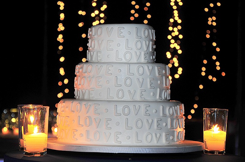 A three-tier wedding cake decorated with the word "LOVE" and surrounded by candles.