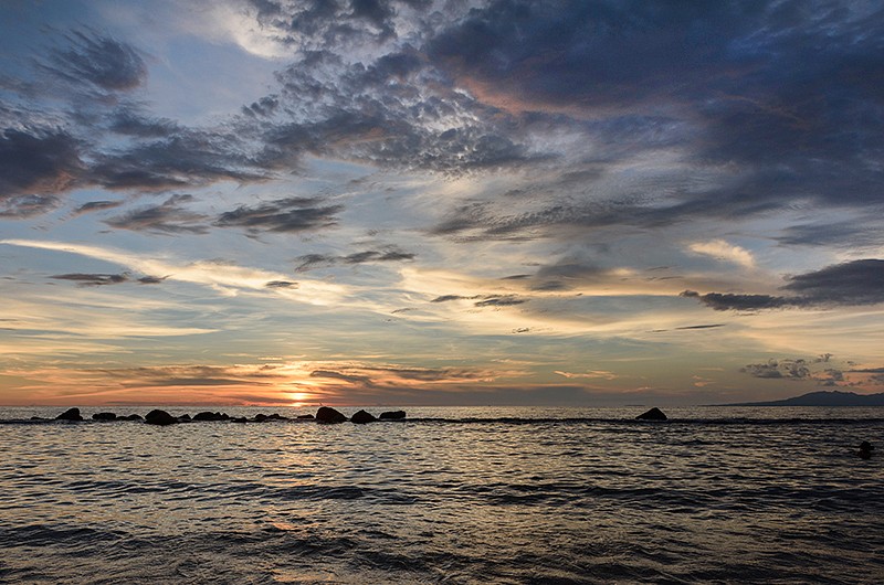 view of the ocean at dusk as the sun sets within the clouds.