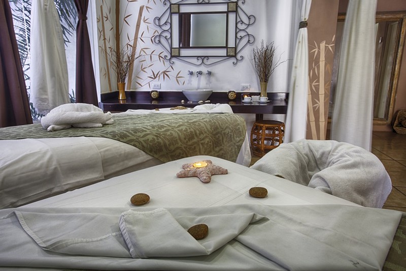 Massage tables with warm tone colored cloth and towels with a candle and rocks.