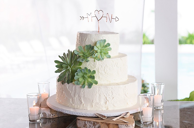 A three-tier wedding cake decorated with succulents and a heart-shaped topper.